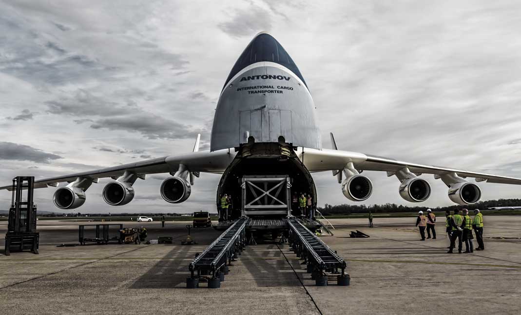International Cargo transporter Antonov aircraft in the airport tarmac unloading cargo goods beeing unloaded by several workers.