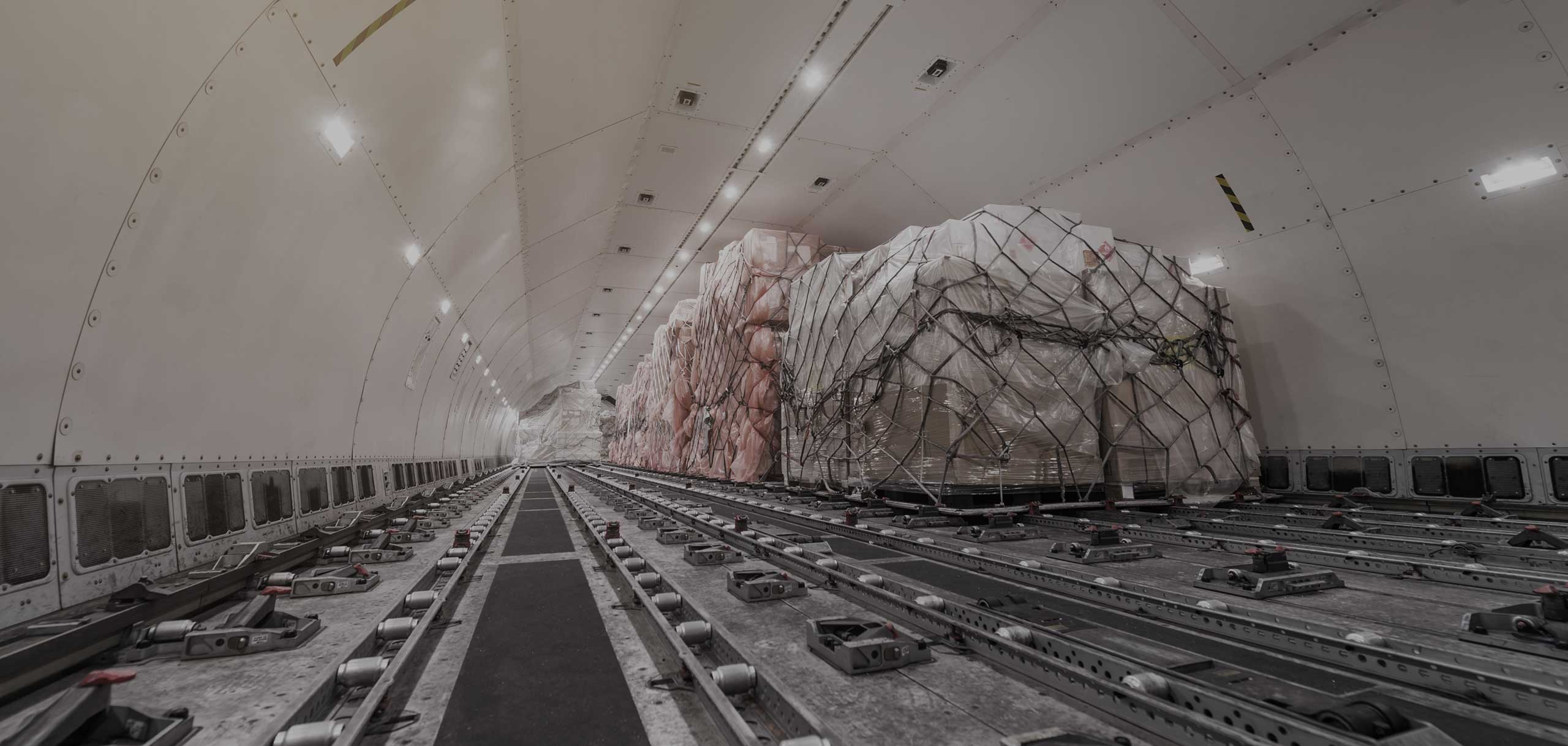 A view from inside an aircraft trunk with containers and pallets goods being loaded.