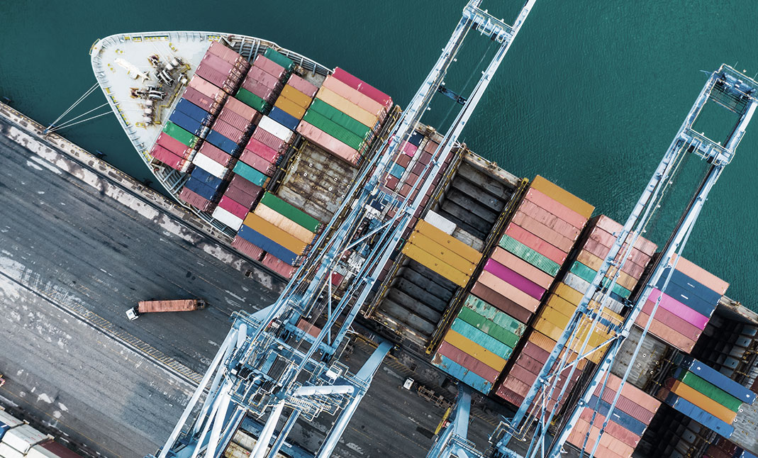 Cargo ship being loaded on the martime port to carry containers on the sea. A maritime crane is loading a container to the cargo ship on the dock.